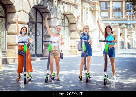 Ragazze con maschere facciali che si divertono guidando scooter elettrici in città Foto Stock