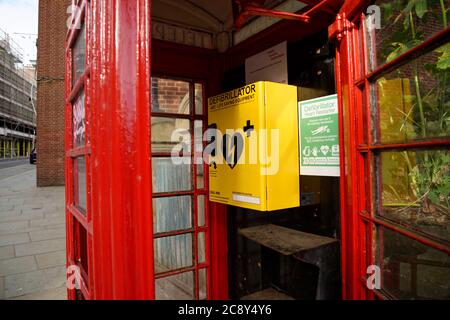 Un defibrillatore in una vecchia scatola telefonica rossa. Foto Stock