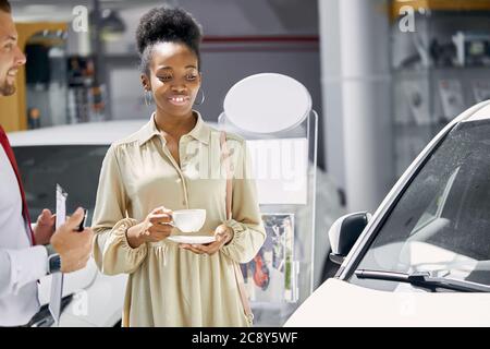 giovane donna afro attraente godere di essere proprietario di nuova auto, signora di affari fare l'acquisto in concessionaria Foto Stock