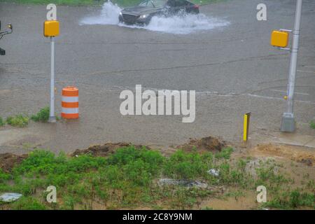 La strada allagata da forti precipitazioni piovose in auto sta guidando attraverso un grande puddle con onde sulla strada durante la giornata della pioggia pesante Foto Stock