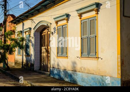 Una casa coloniale portoghese con persiane blu e finiture gialle e piastrelle blu intorno alla porta ad arco. Foto Stock
