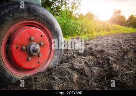 Pneumatico anteriore del trattore nel terreno al tramonto, messa a fuoco selettiva, concetto di lavoro sul campo. Foto Stock