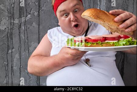 WOW grasso uomo è sorpreso di un grande sandwich, lo apre e guarda all'interno. Bel ragazzo divertente vuole mangiare dopo l'allenamento sportivo Foto Stock