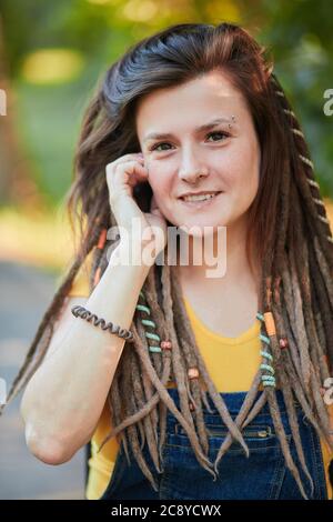 Bella caucasica cool ragazza con Dreadlock, naso piercato in una T-shirt gialla e una generale blu godendo calde giornate estive. Primo piano ritratto. Foto Stock