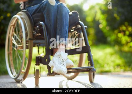 giovane ragazza disabile in tuta e trainer bianchi seduti con gambe incrociate sulla sedia a rotelle. primo piano foto ritagliata. Foto Stock