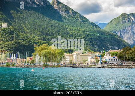 Riva del Garda porto con barche situato presso il lago di Garda, alte montagne sullo sfondo, giornata di sole Foto Stock