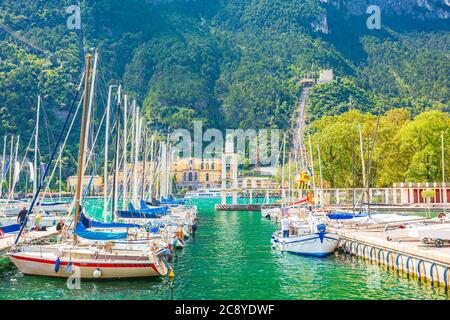 Riva del Garda porto con barche situato presso il lago di Garda, alte montagne sullo sfondo, giornata di sole Foto Stock