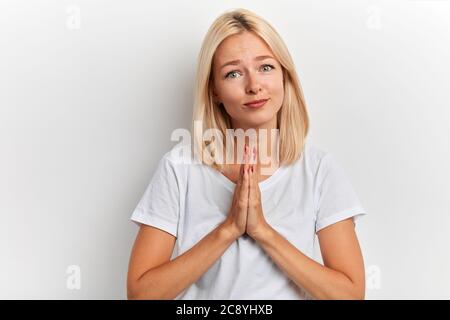 gentile donna dai capelli giusti, amichevole prega per il benessere della sua famiglia, tiene le palme pressate insieme, su sfondo bianco. Persone, fede, speranza, aiutami Foto Stock