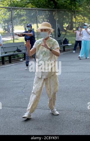 Uomini e donne di varie età ed etnie frequentano una lezione di Tai Chi al mattino indossando maschere chirurgiche e divaricatori sociali. In Queens, New York City. Foto Stock