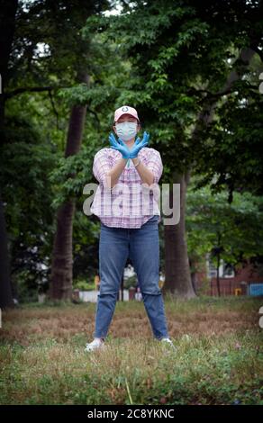 Una donna asiatica americana, probabilmente cinese assiste una classe esterna di Tai Chi mentre indossa una maschera chirurgica e guanti di gomma. A Flushing, Queens, New York Foto Stock