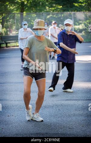 Uomini e donne di varie età ed etnie frequentano una lezione di Tai Chi al mattino indossando maschere chirurgiche e divaricatori sociali. In Queens, New York City. Foto Stock