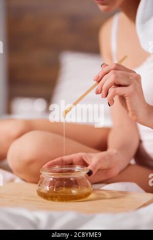 Le mani giovani femmina che tengono il vaso di vetro e bastone di legno, lo zucchero liquido che scorre giù dal bastone, la donna che prepara tutto per lo zuccheraggio, la bellezza b Foto Stock