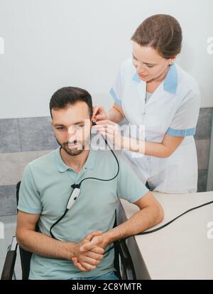 Diagnosi di compromissione dell'udito, timpanometria, test uditivo. Un uomo durante una procedura diagnostica uditiva e un auricolare speciale nell'orecchio. Foto Stock