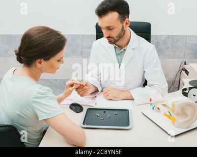 Un giovane audiologo seleziona un apparecchio acustico per una donna caucasica. la paziente ha bisogno di buoni apparecchi acustici in modo da poter sentire i suoni del mondo. Foto Stock