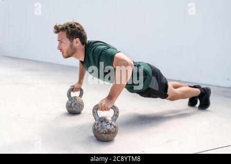 Fitness man facendo push-up tenendo su kettlebells Foto Stock