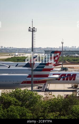 Stabilizzatori verticali di vari aeromobili parcheggiati in un'area remota di Sao Paulo/Guaruhos Intl. Aeroporto, mentre il traffico a terra sta tassando in background. Foto Stock