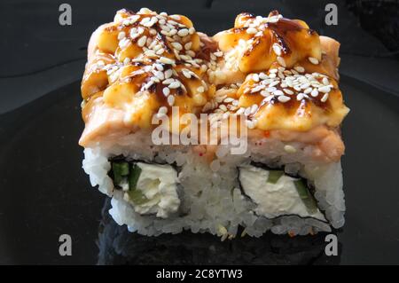 Il sushi giapponese sul piatto nero. Panini caldi al forno con tonno, salmone, gamberi, granchio e avocado. Vista dall'alto del sushi assortito. Foto Stock