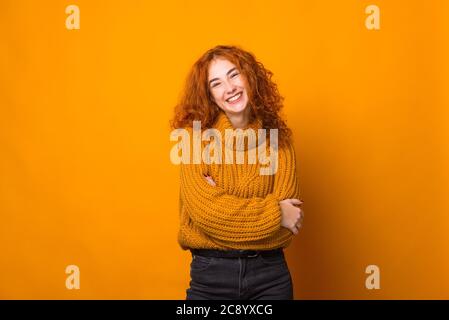 Foto di carino redhead girl, guardando la fotocamera con toothy smle, mani piegate, seduto su sfondo arancione Foto Stock