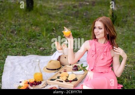 Sorridente giovane ragazza nel parco che tiene un drink, facendo un picnic estivo in un parco all'aperto. Cibo sano, concetto di relax Foto Stock