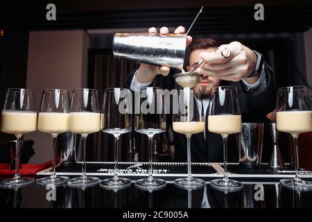 mani di un barman che tiene un agitatore che versa una bevanda in un bicchiere Foto Stock