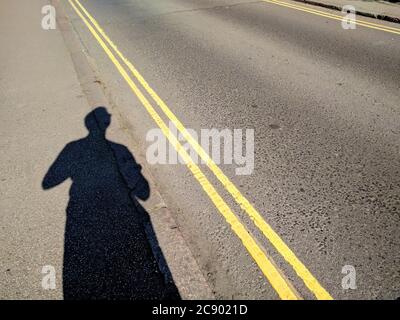 Ombra di figura su Hot Tarmac Asphalt Road con doppie linee gialle Foto Stock