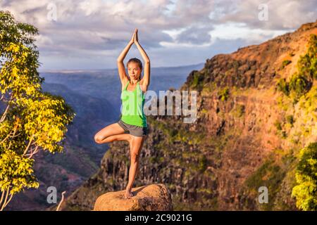 Yoga Serena donna meditando facendo albero posa Vriksasana su paesaggio di montagna natura. Donna che pratica la meditazione al tramonto, sano stile di vita attivo Foto Stock