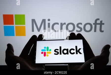 Stone / Regno Unito - Luglio 27 2020: Logo slack visto sulla silhouette dello smartphone in mani e logo Microsoft sullo schermo sfocato dietro. Concetto per Slac Foto Stock