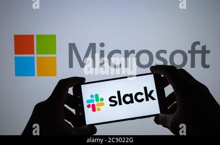 Stone / Regno Unito - Luglio 27 2020: Logo slack visto sulla silhouette dello smartphone in mani e logo Microsoft sullo schermo sfocato dietro. Concetto per Slac Foto Stock