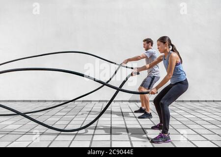 Fitness persone che si esercitano con corde di battaglia in palestra. Donna e uomo coppia allenarsi insieme facendo combattimento corda allenamento lavorando le braccia e cardio per Foto Stock