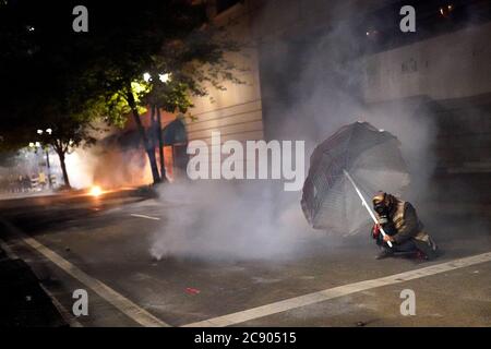 Portland, OREGON, Stati Uniti. 27 luglio 2020. Un protestore si copre dietro un ombrello da prato mentre gli ufficiali federali sparano gas lacrimogeni per disperdere una protesta contro l'ingiustizia razziale e la brutalità della polizia di fronte al tribunale Mark O. Hatfield a Portland, Ore., il lunedì mattina 27 luglio 2020. Credit: Nathan Howard/ZUMA Wire/Alamy Live News Foto Stock