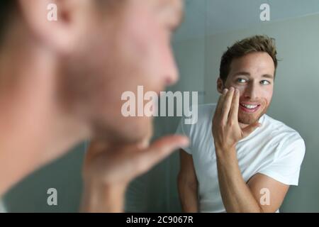 Crema per il viso giovane uomo mettendo prodotto di bellezza per la pelle idratante per il viso. Trattamento viso di bellezza maschile cura a casa stile di vita. Persona che chiede Foto Stock