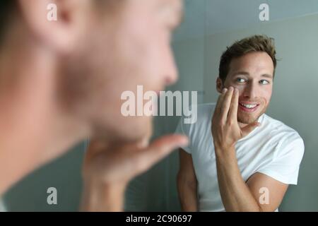 Crema per il viso giovane uomo mettendo prodotto di bellezza per la pelle idratante per il viso. Trattamento viso di bellezza maschile cura a casa stile di vita. Persona che chiede Foto Stock