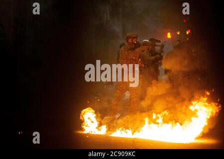 Portland, Oregon, Stati Uniti. 27 luglio 2020. Gli ufficiali federali passano davanti a un piccolo incendio e disperdono una protesta contro l'ingiustizia razziale e la brutalità della polizia davanti al tribunale Mark O. Hatfield a Portland. Credit: Nathan Howard/ZUMA Wire/Alamy Live News Foto Stock