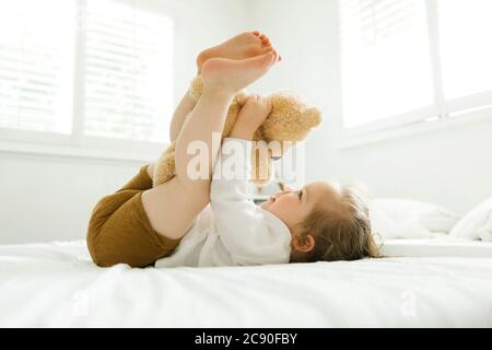 Bambina sdraiata sul letto con il suo giocattolo da orsacchiotto Foto Stock