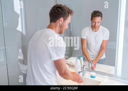 Giovane uomo che lava le mani a casa lavando la mano sotto l'acqua corrente nel lavandino del bagno. Casa, appartamento condominio stile di vita di lusso Foto Stock