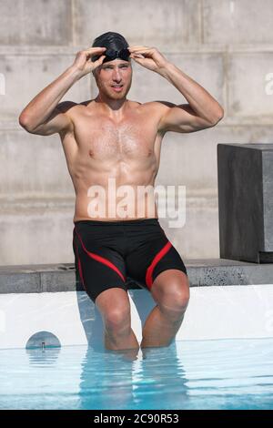 Atleta nuotatore si prepara per la gara indossare occhiali di protezione e berretto per la gara di nuoto allo stadio della piscina al coperto. Giovane m Foto Stock