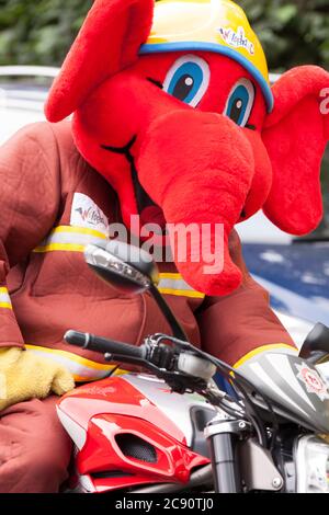 La mascotte di sicurezza Burn Trust per bambini Welefant arriva alla stazione dei vigili del fuoco di Bridport sulla sua moto Aprilia. Foto Stock