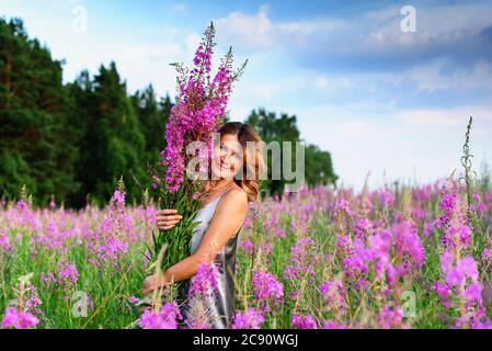 Bella donna in abito grigio si rilassa con mazzo di fiori sul prato di fireweed Foto Stock