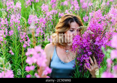 Bella donna in abito grigio si rilassa con mazzo di fiori sul prato di fireweed Foto Stock