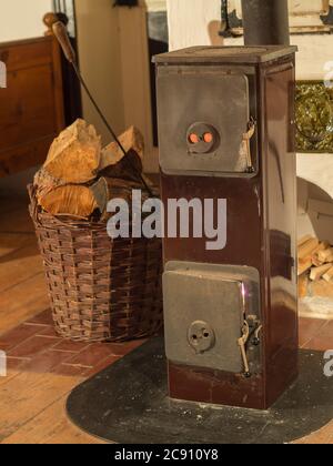 vecchia stufa a legna con cesto di vimini pieno di legno tagliato e fuoco-uncino sul pavimento di legno in legno in legno cottage in legno Foto Stock