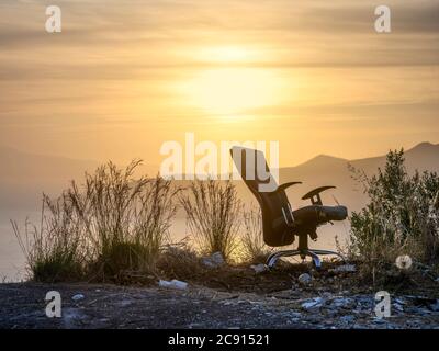 Una sedia da ufficio abbandonata in un paesaggio tramonto. Foto Stock