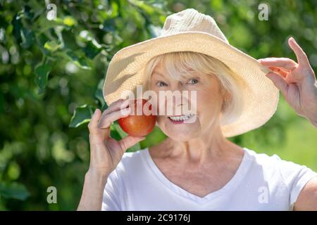 Donna sorridente che indossa un cappello e tiene una mela rossa Foto Stock
