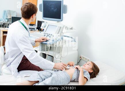 Medico che guarda il monitor mentre esegue la scansione ecografica su una ragazza di dieci anni Foto Stock