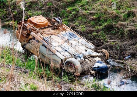 La vecchia automobile arrugginita è stata girata in un fiume tra i campi, inquinando l'ambiente Foto Stock