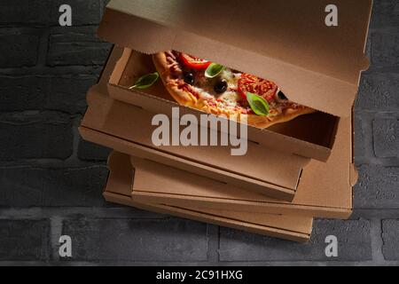 Pizza italiana confezionata pronta per l'uso in una scatola da asporto di cartone marrone sopra un ordine accatastato su piastrelle nere Foto Stock