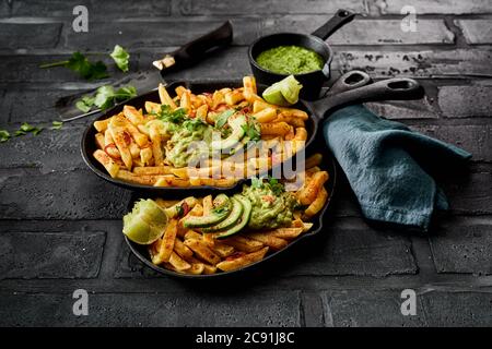 Due esperti con porzioni di patatine salate al forno o fritte condite con pera di avocado fresca e salsa di guacamole messicana su un paese piastrellato nero Foto Stock