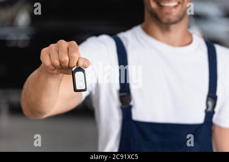 vista ritagliata di un meccanico felice in uniforme tenendo chiave auto Foto Stock