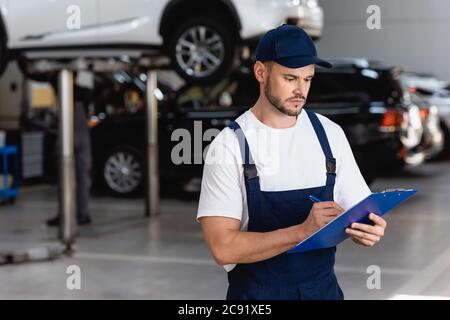 bel meccanico in tute e berretto scrittura mentre tenendo gli appunti Foto Stock