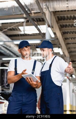 meccanica bella in uniforme utilizzando tablet digitale e gesturing in officina Foto Stock