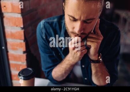 fuoco selettivo di uomo d'affari pensivo che parla sullo smartphone vicino alla tazza di carta con il caffè in movimento Foto Stock